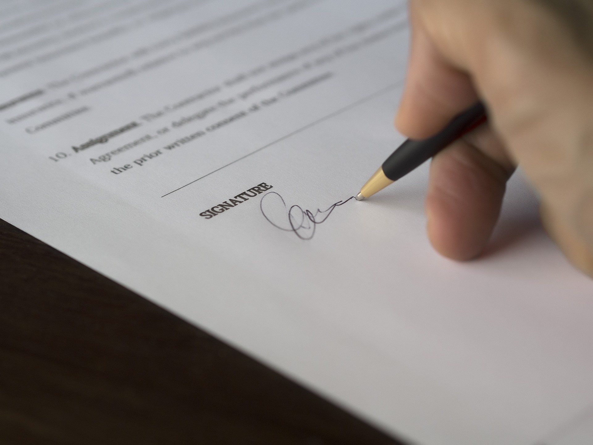 a person's hand signing a contract - Top First Time Home Buyer FAQ’s Answered