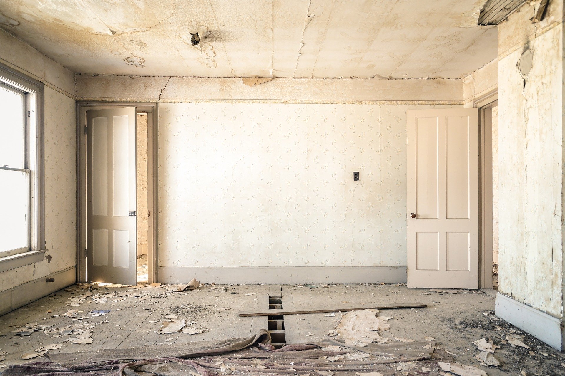 rundown room in a home with floor boards missing and paint peeling