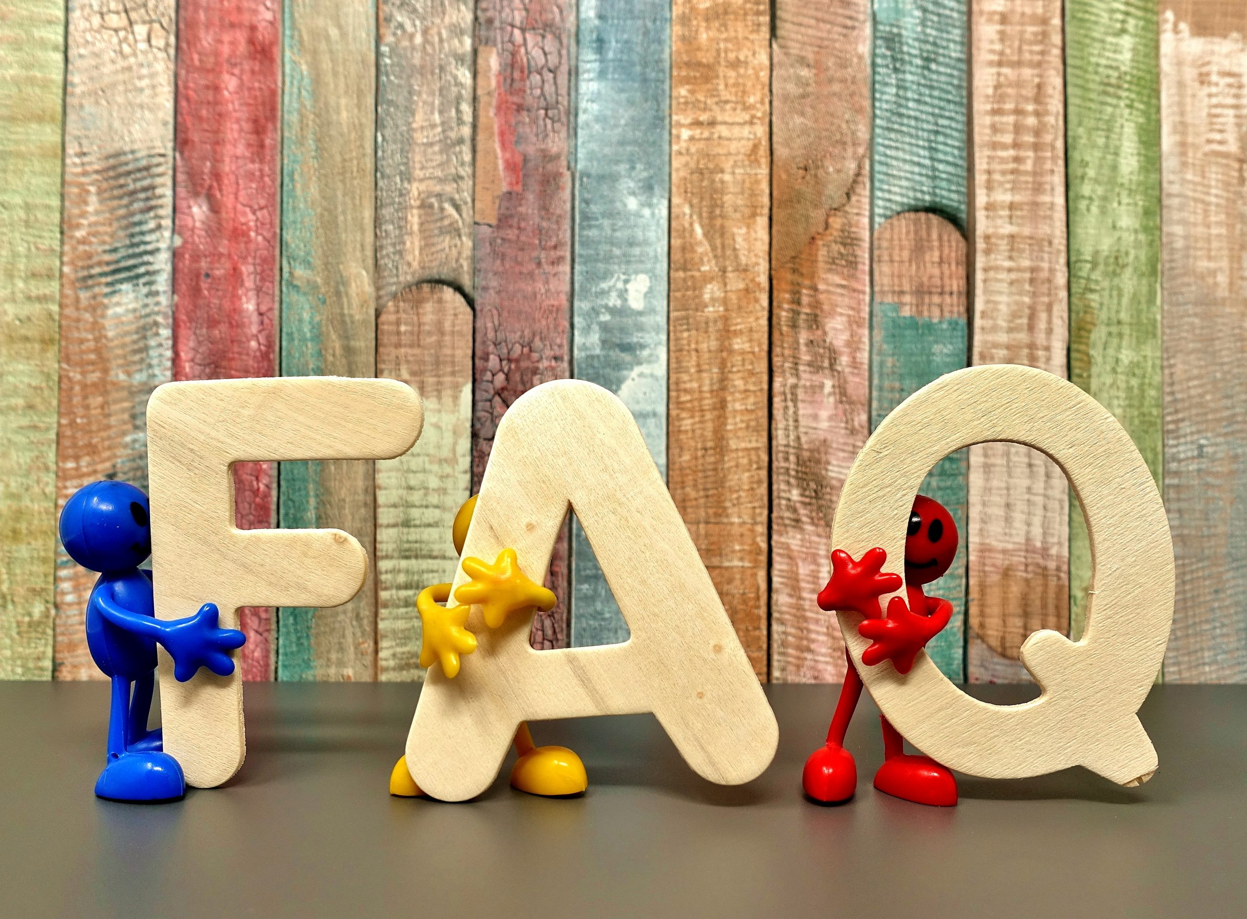 FAQ text that looks like wooden cutouts in front of a colorful wooden back drop with 3 little 3D stick figured people, one colored red, the other yellow and the last blue