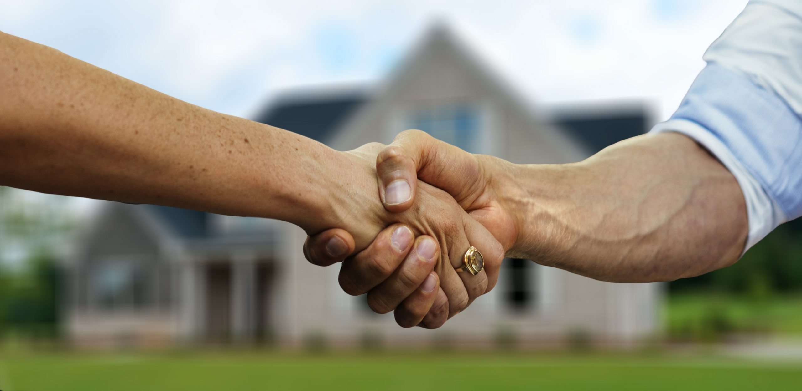 two people shaking hands in front of a house