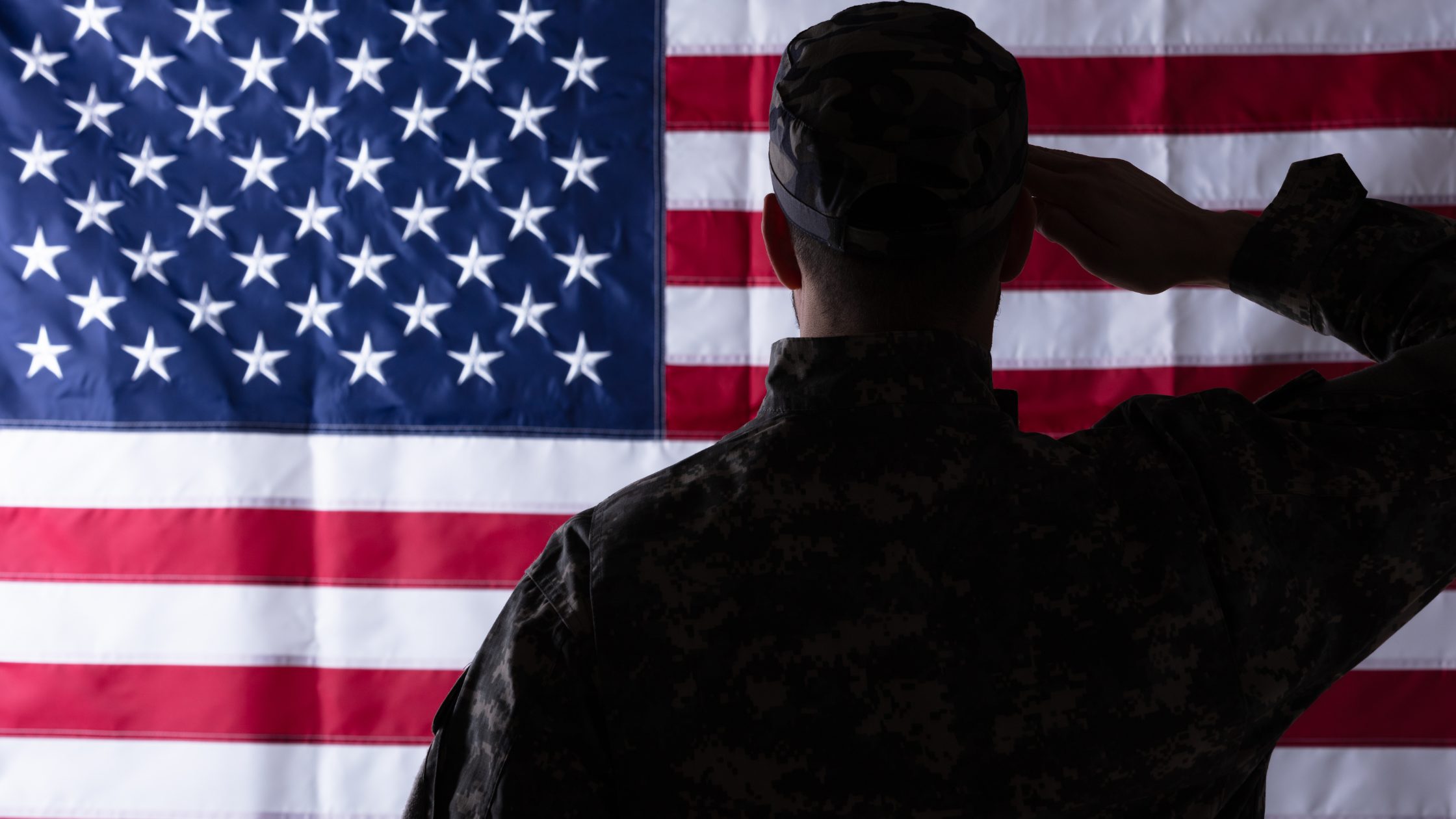 Silhouette of military man saluting in front of the American flag.